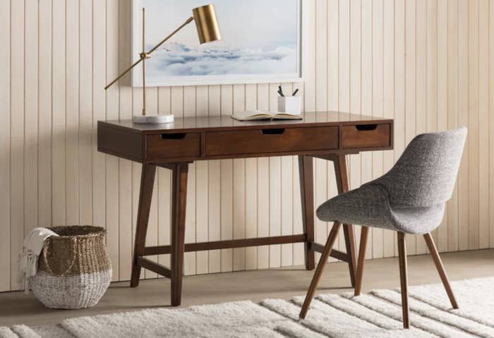 The dark brown desk has one large rectangular drawer and two smaller ones, and it&#x27;s situated in a boho and neutral-colored room
