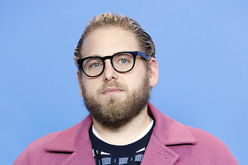 Jonah Hill poses on the red carpet while wearing glasses and a coat and sweater