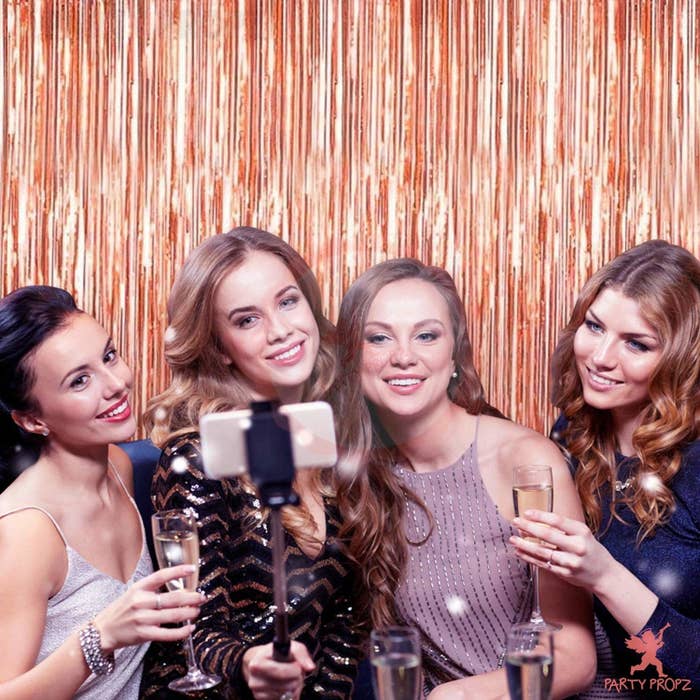 4 women standing in front of a rose gold foil curtain clicking selfies