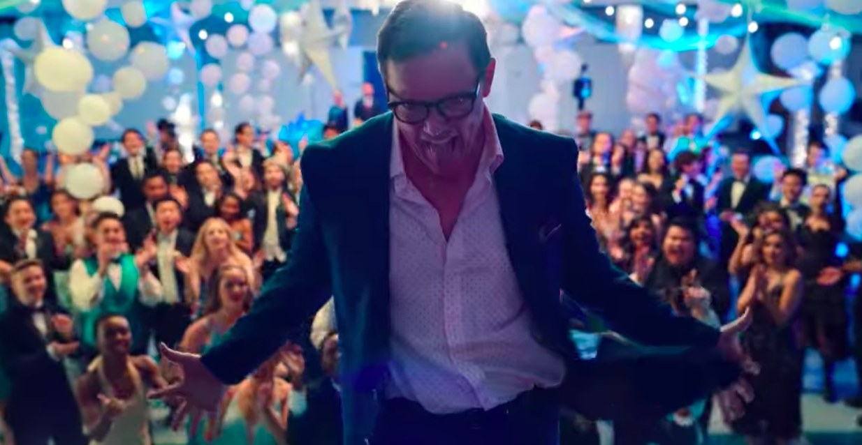 Matthew Lillard dances on a stage in front of a group of students at prom