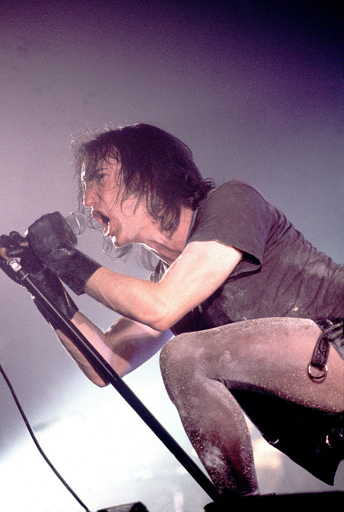 Reznor dressed in black, leaning over a mic and singing