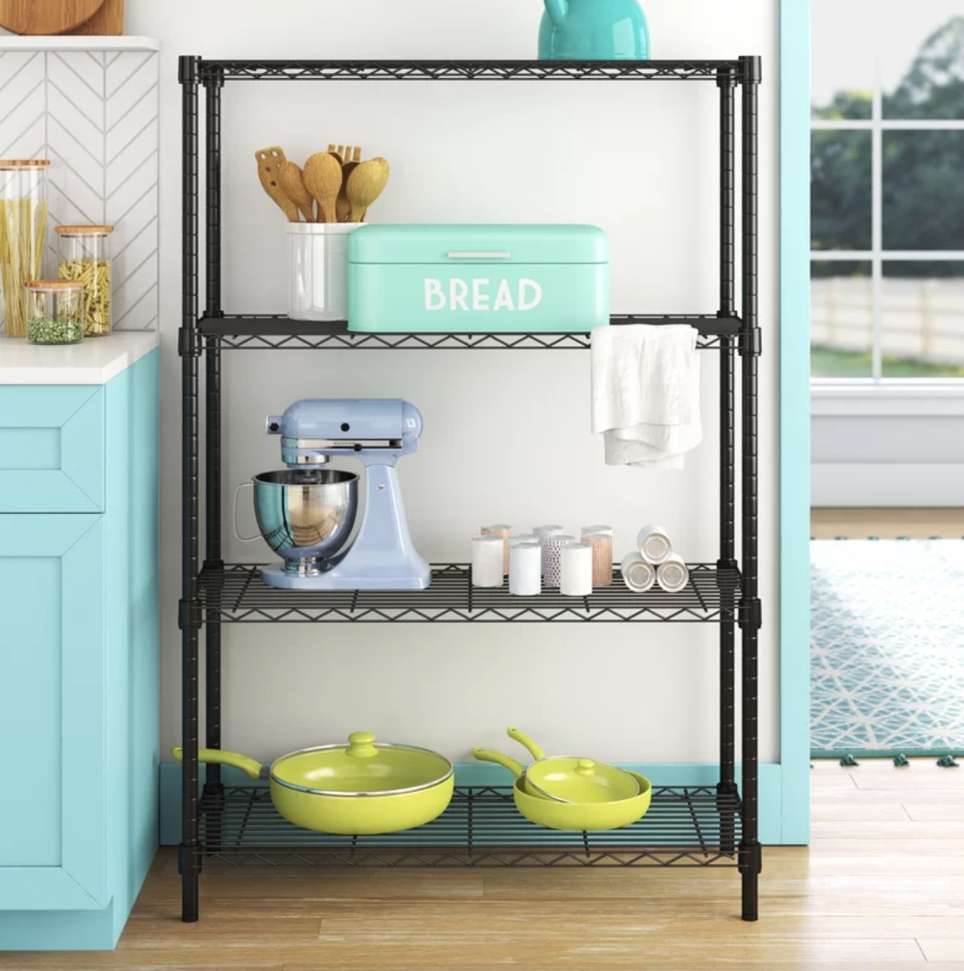 The black wire shelving unit is in a kitchen and is holding pastel-colored items such as pots and other kitchen tools