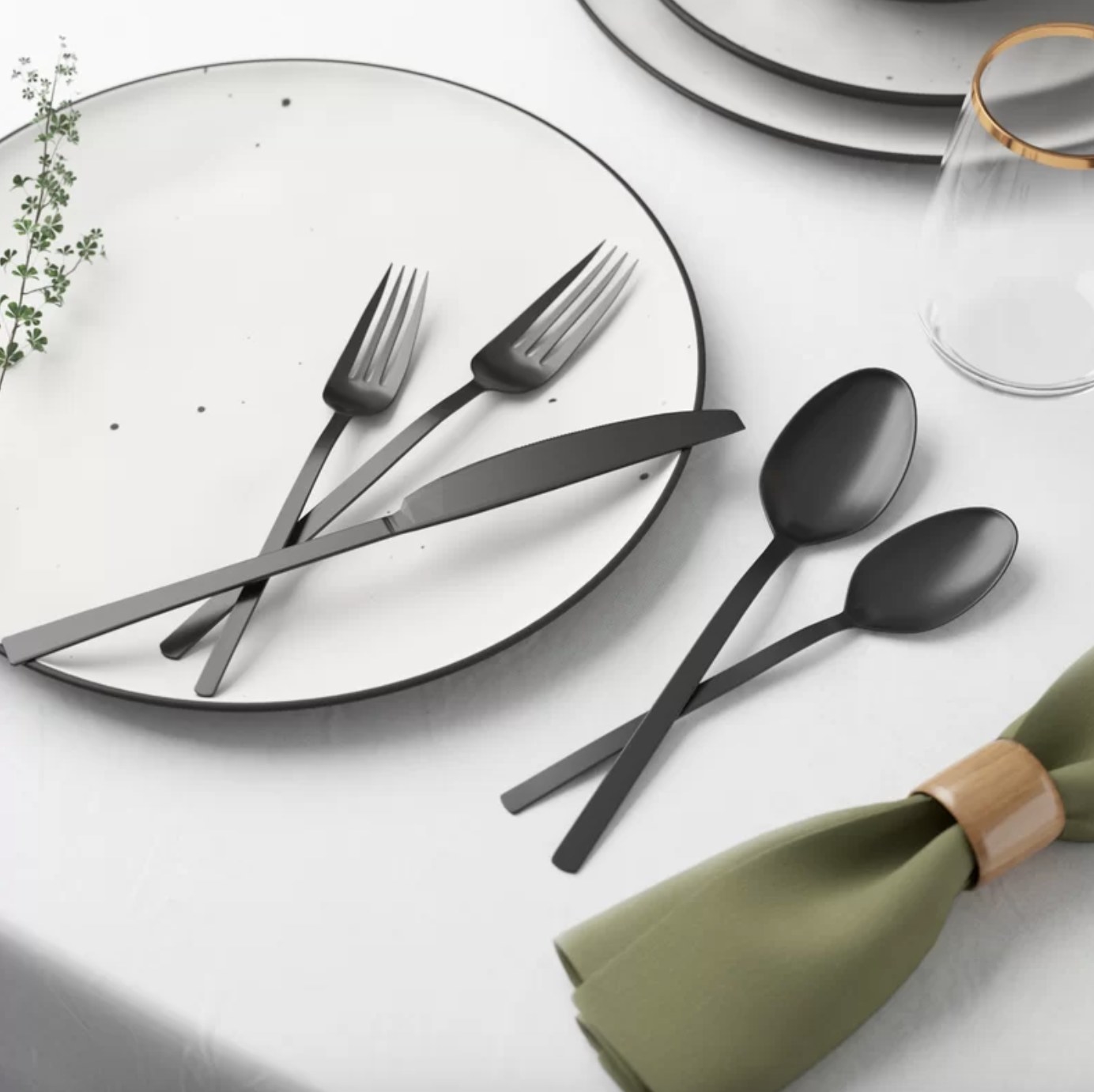 There is one black dinner fork, salad fork, dinner kife, soup spoon and a teaspoon laid across a white plate.