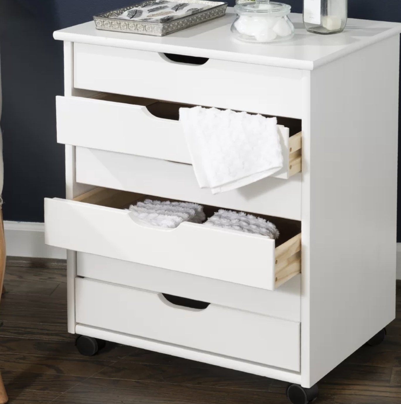 The vertical shelf unit is white and and has six rectangular pull-out drawers