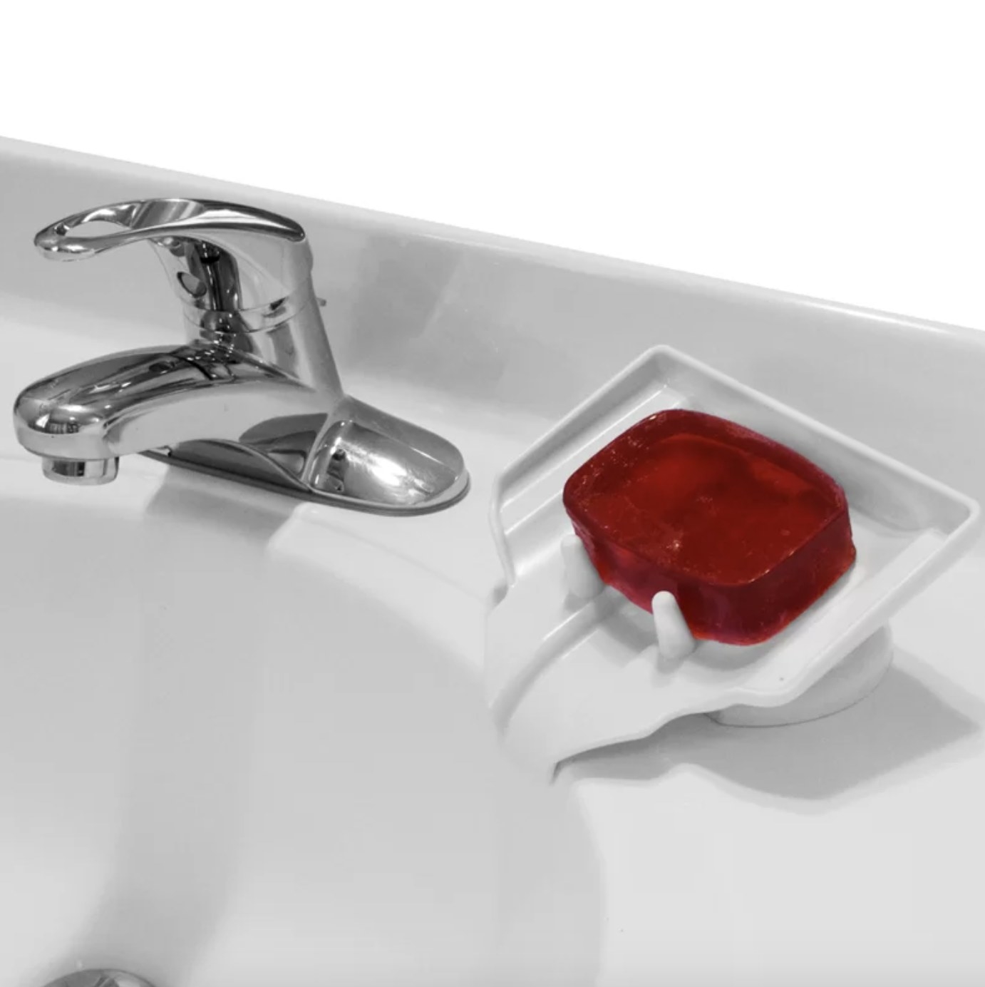 A bright red bar of soap sits atop the white soap saver with a curved waterfall spout and angled rectangular tray with two white stoppers