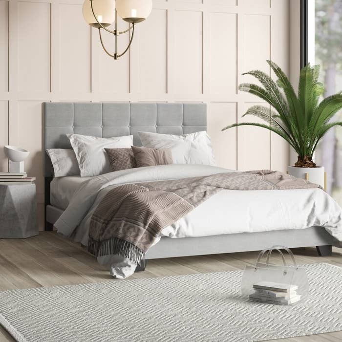 The bed in gray decorated with pillows and blankets