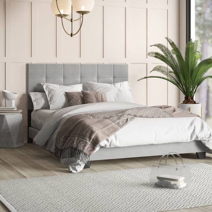 The bed in gray decorated with pillows and blankets