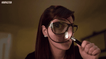A woman holds up a magnifying up to her eye, which obscures most of her face, showing only one bespectacled eye