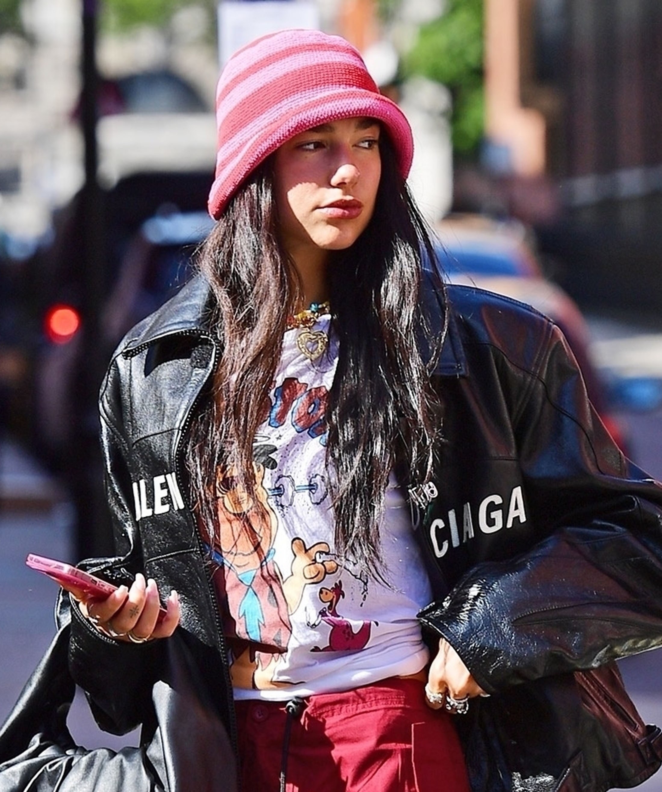 Dua looking to the side while wearing a black jacket and cartoon T-shirt and holding a cellphont