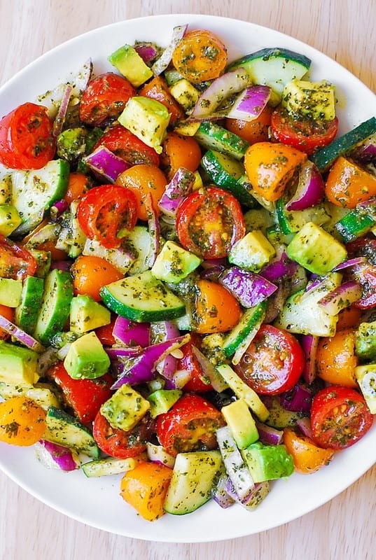 A cucumber, avocado, red onion, and tomato salad with pesto.