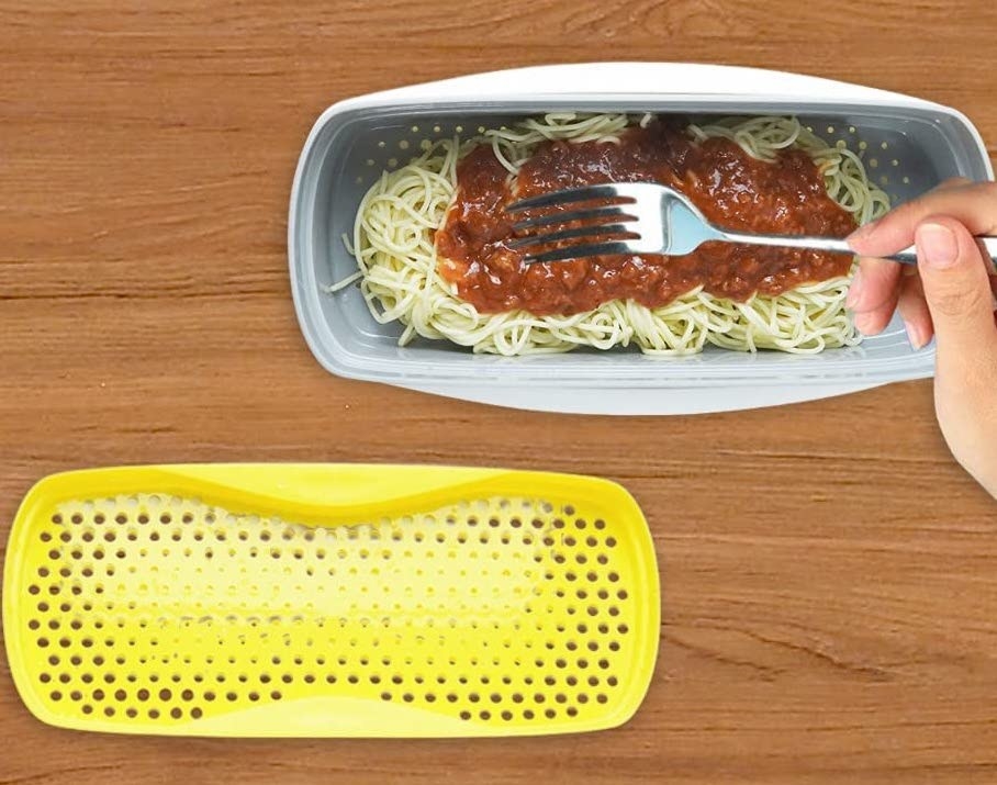A person using a fork to mix spaghetti in the container