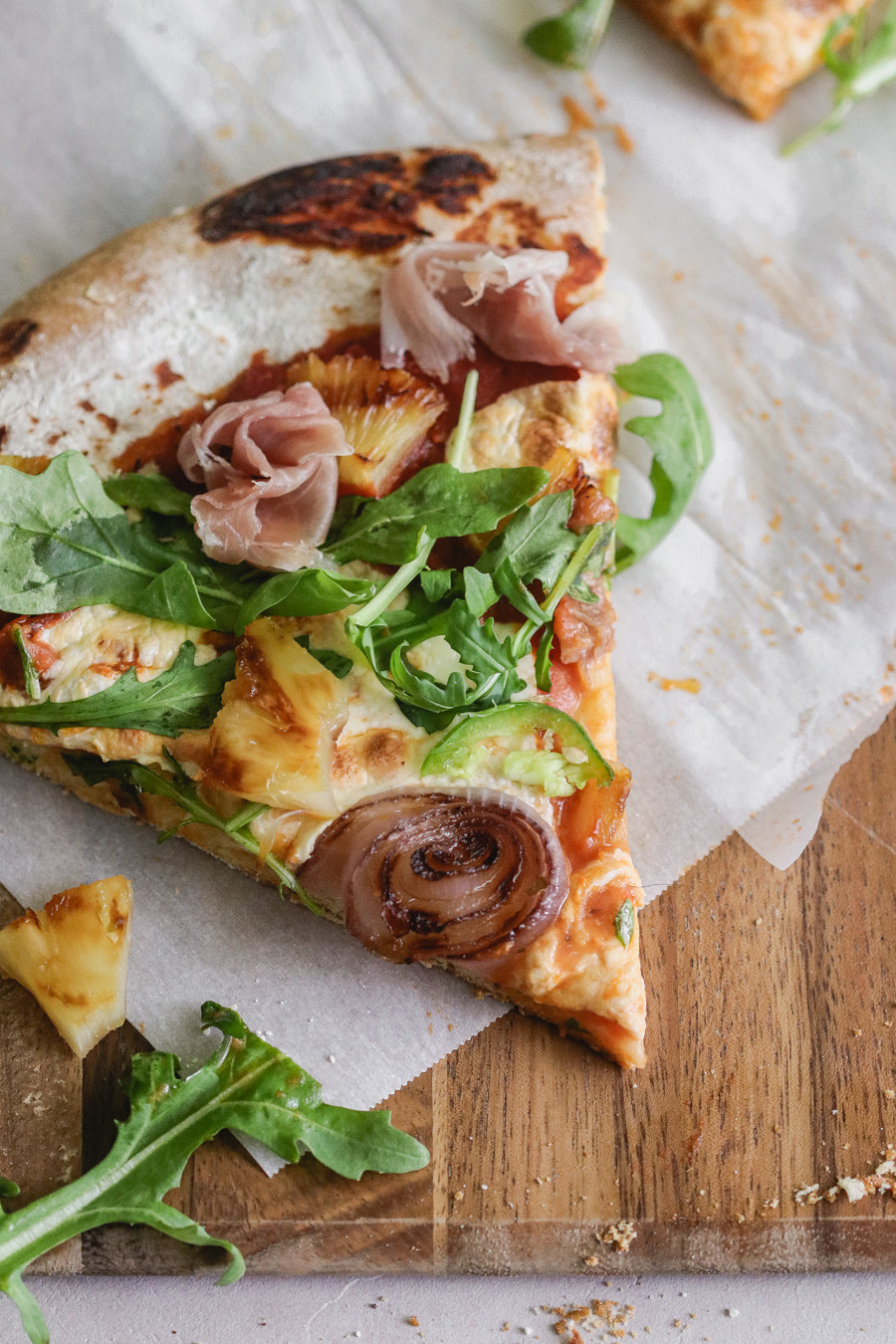 A slice of pizza with arugula, pineapple, and prosciutto.
