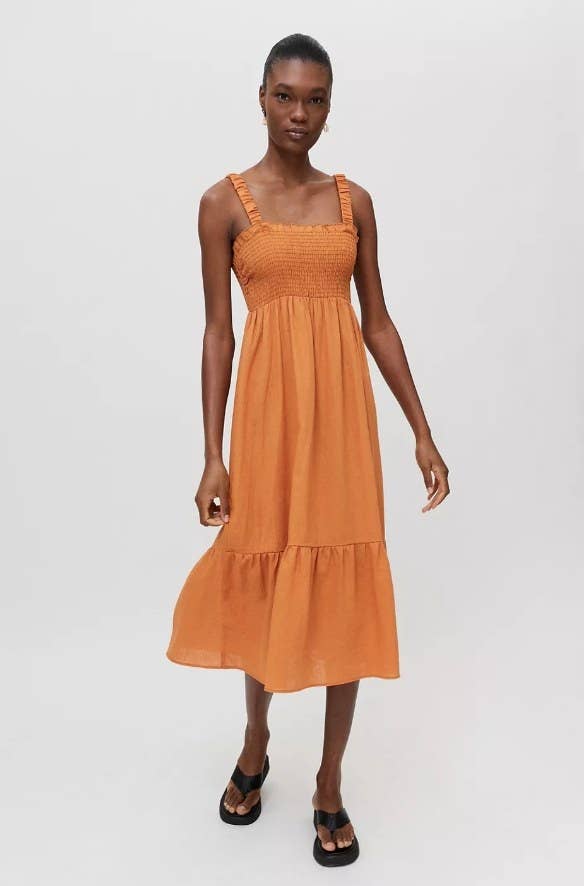 Model wearing orange mid-length smock dress with black sandals