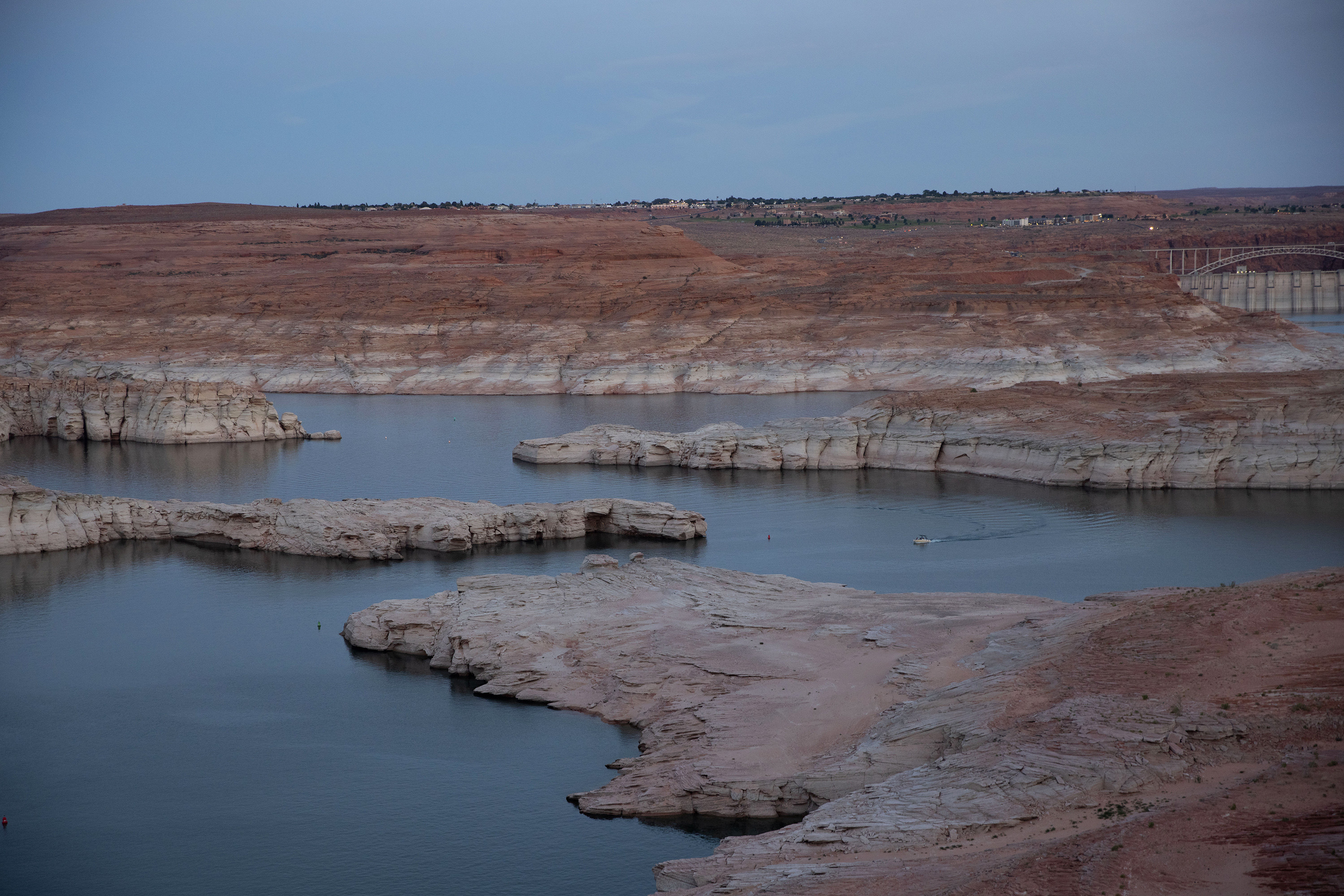 Low water levels are seen at dusk in Lake Powell with urban development in the background as a boat moves through the body of water