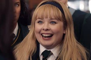 clare from derry girls wears a headband, has her eyes and mouth wide open as if excited