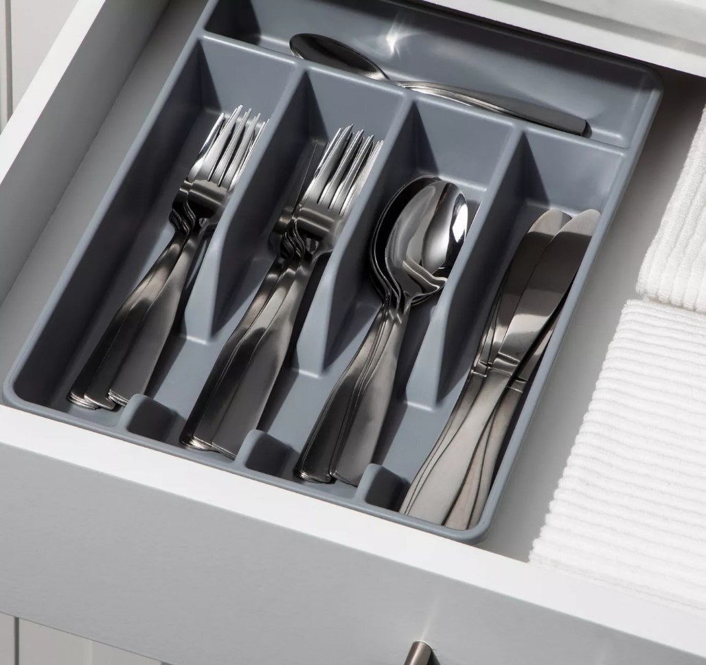 A gray utensil organizer filled with spoons, knives, and forks