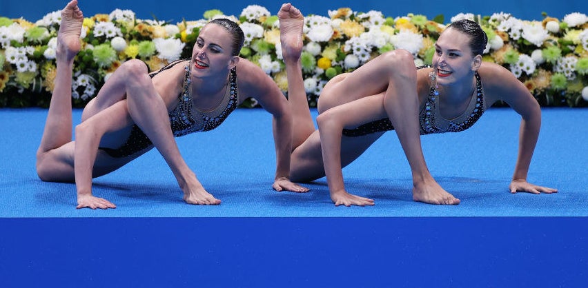 The synchronized swimmers each have a leg twisted over an arm as they crouch on the ground
