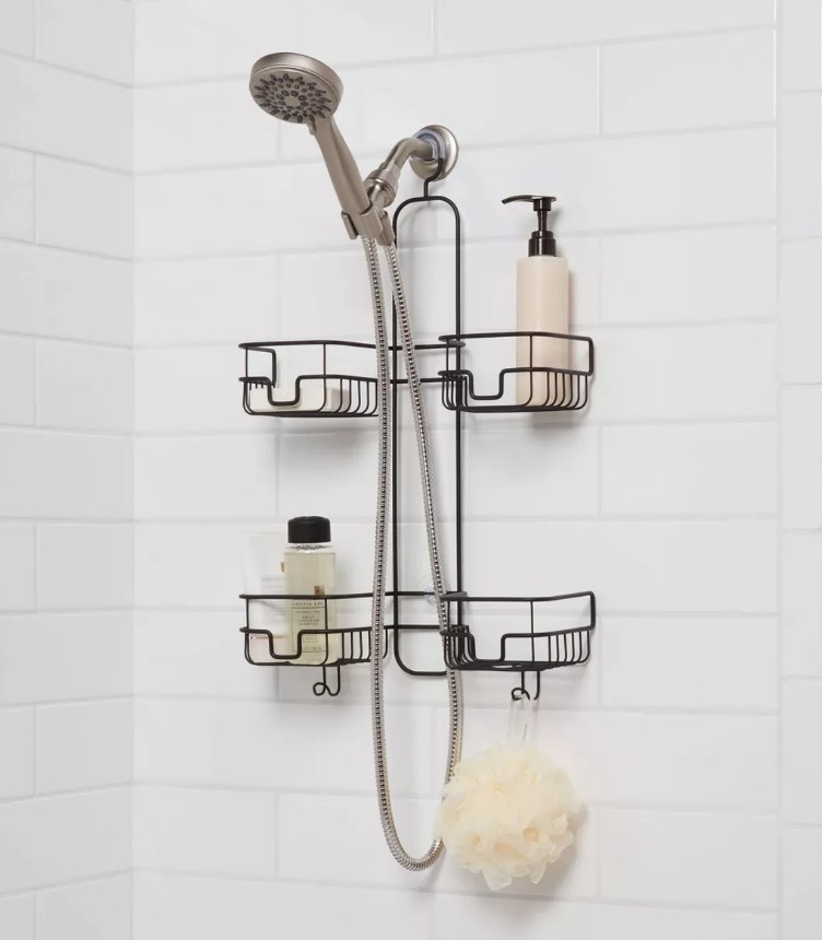 A black, metal shower caddy hanging over the shower head filled with soaps with a loofa hanging off the bottom hook