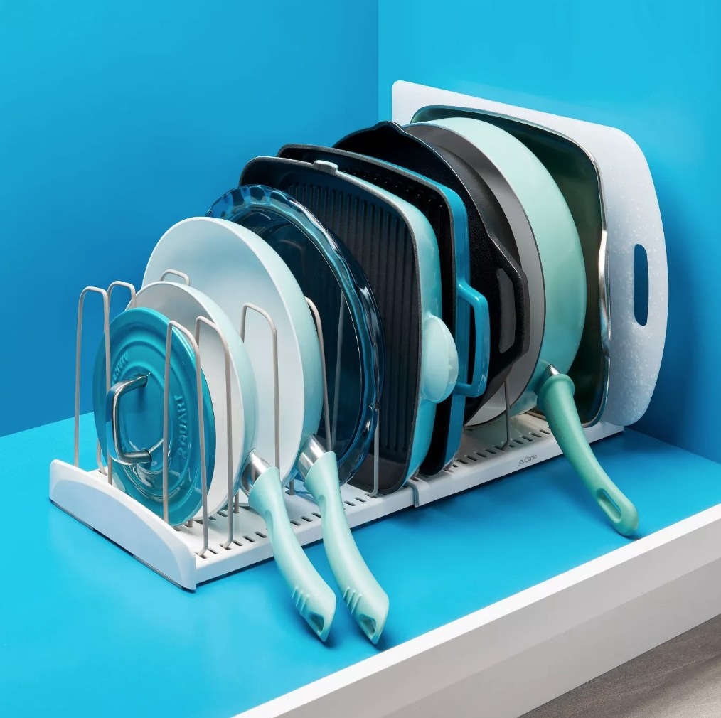 An expandable cookware rack filled with pots, pants, cake tins, griddles, and cutting boards