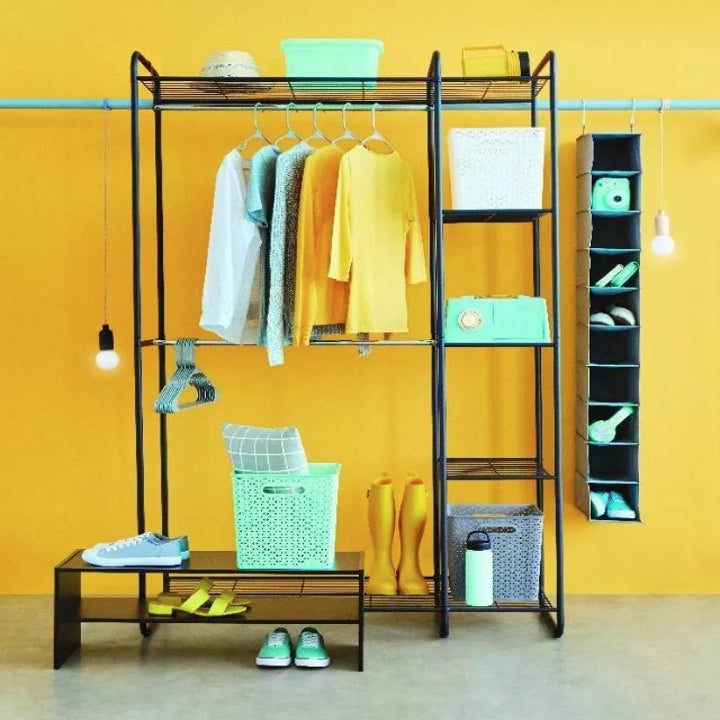 A black/silver, freestanding closet rack with five shelves, and two hanging rods filled with clothing