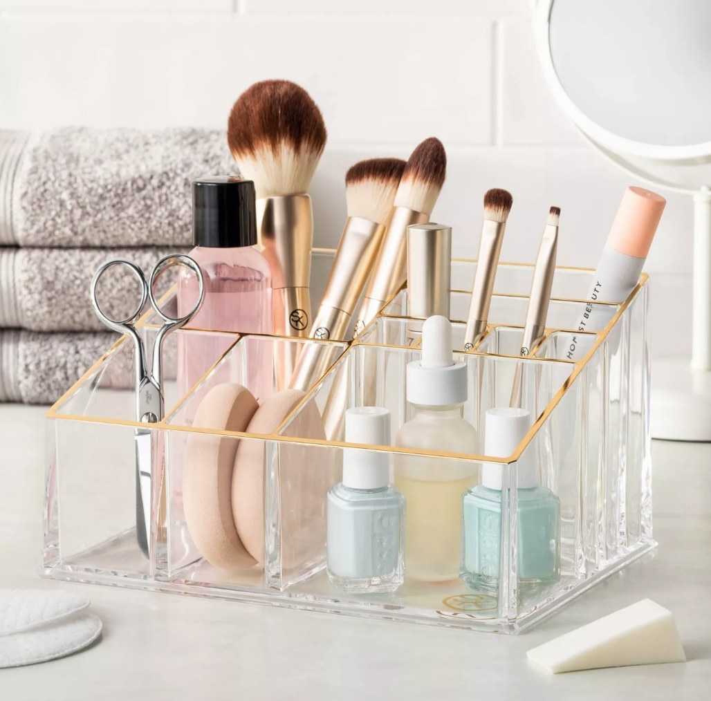 A clear makeup organizer with ten compartments filled with nail polish, brushes, mascara, and more makeup products