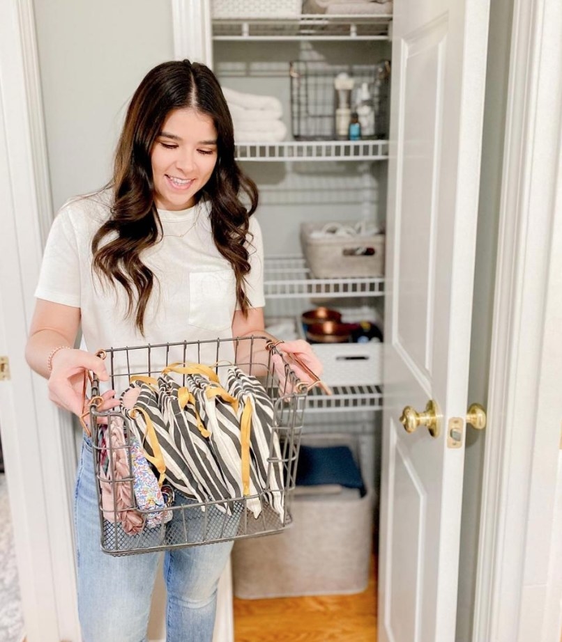 A model holding a gray, stackable wire basket with handles in front of a linen closet