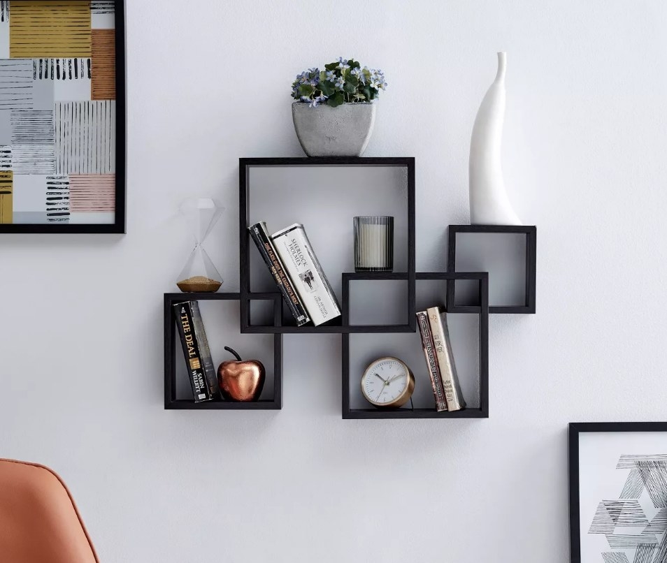 A black, geometric shelf unit mounted to a wall filled with books, plants, and decor items