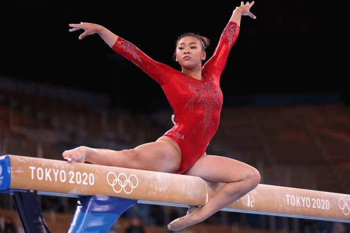 Suni Lee posing on the balance beam with her hands in the air