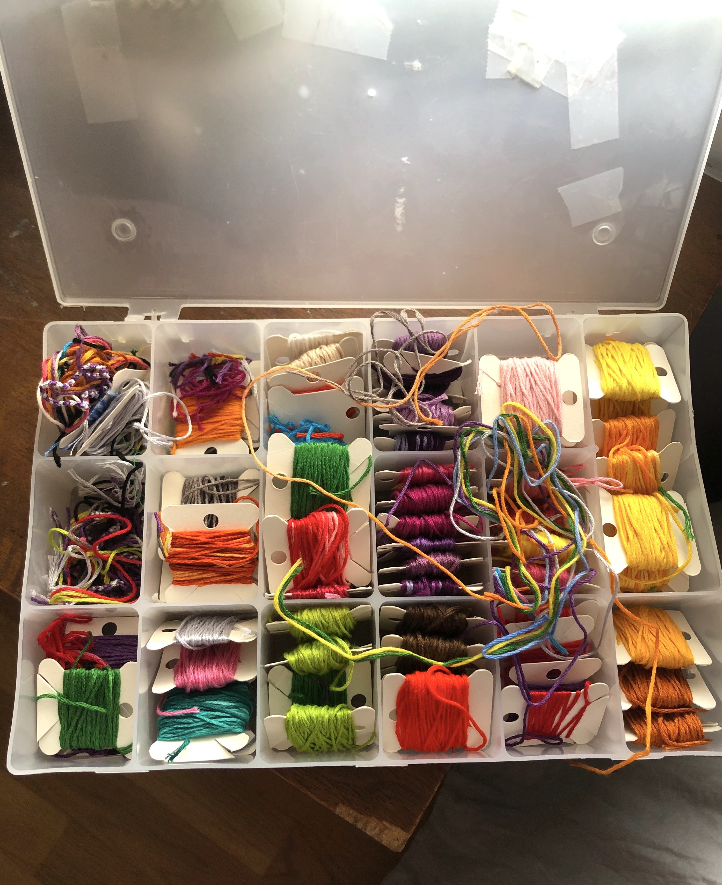 Rolls of colorful string wrapped around paper squares in a plastic box