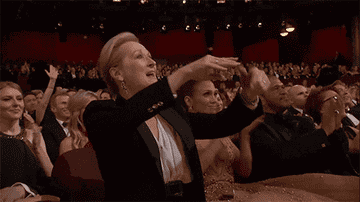 Meryl Streep standing up, clapping, and pointing at the Oscars