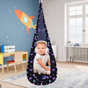 A child wearing head phones and sitting in the pod swing in unicorn print
