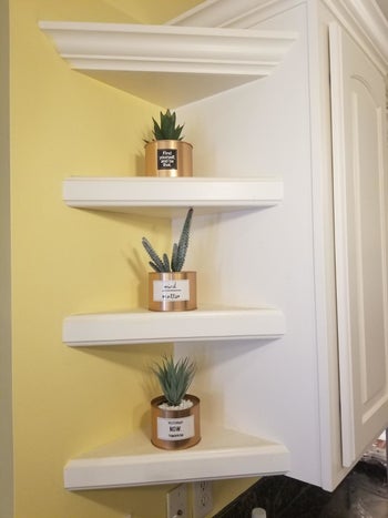 Reviewer's photo showing the three gold artificial succulent planters displayed on shelves against a yellow wall