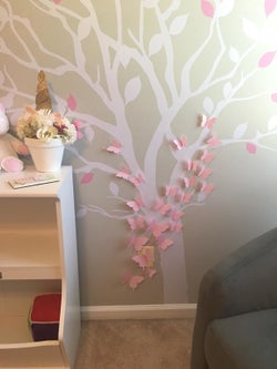Reviewer's photo showing the pink butterfly stickers  arranged on a tree decal on the wall