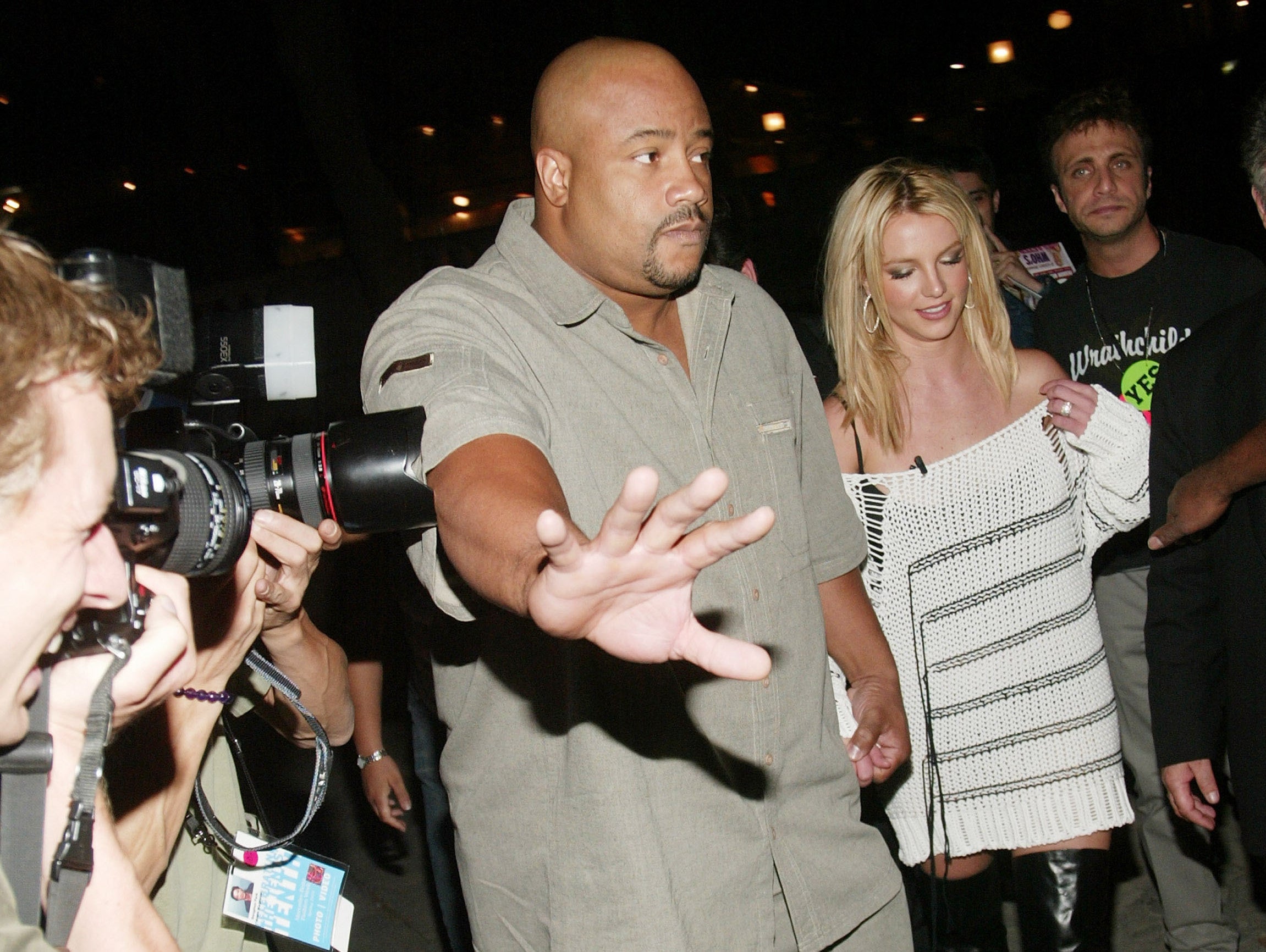 A bodyguard pushes cameras away from Britney while she walks down a street