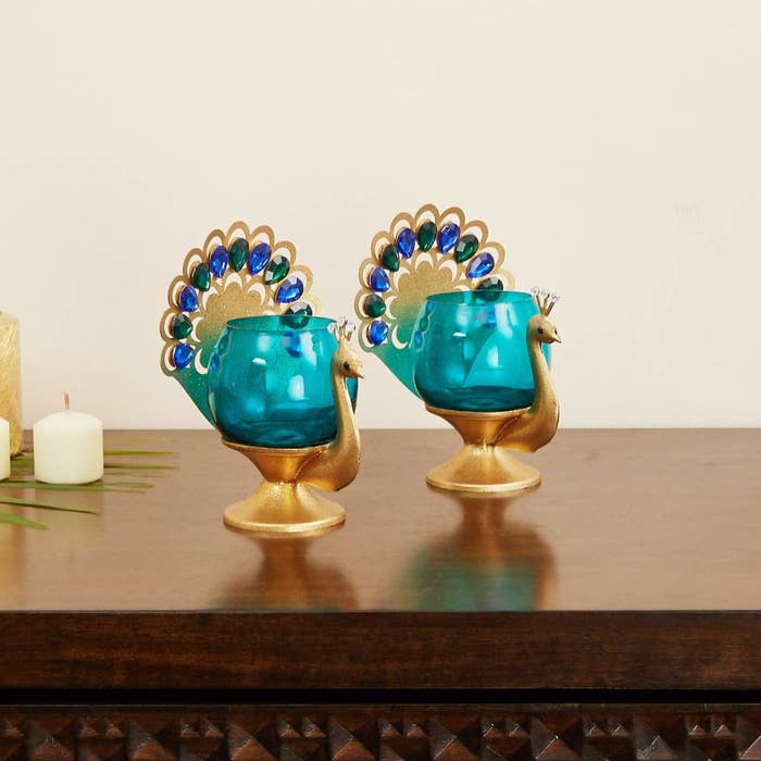 A pair of peacock tealight holders on a table next to a candle