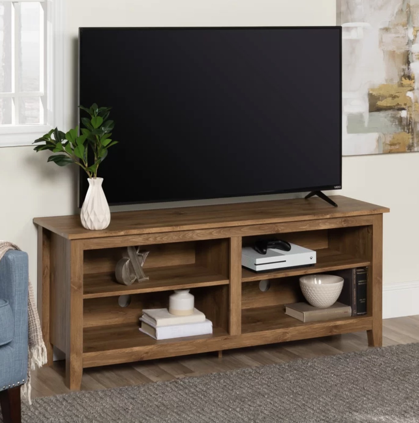 The barn wood colored stand is holding various decor items and a large black TV on top