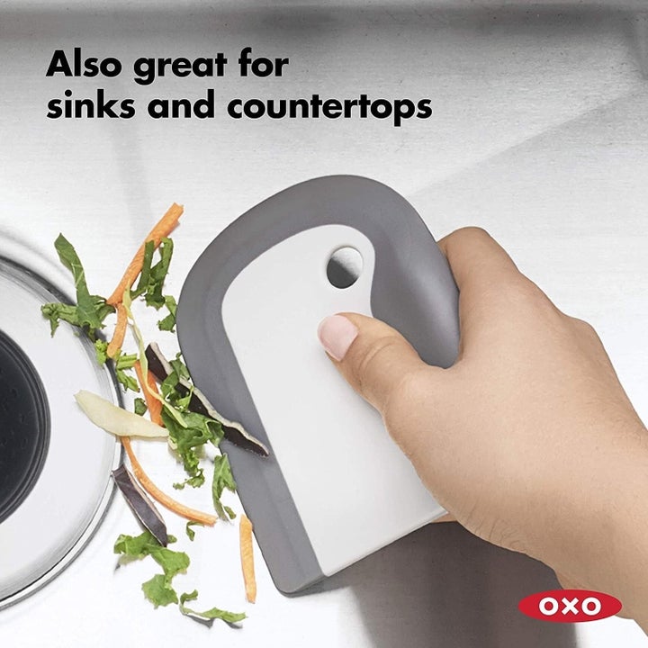 hand using the tool to push scraps into the garbage disposal with the text "also great for sinks and countertops"