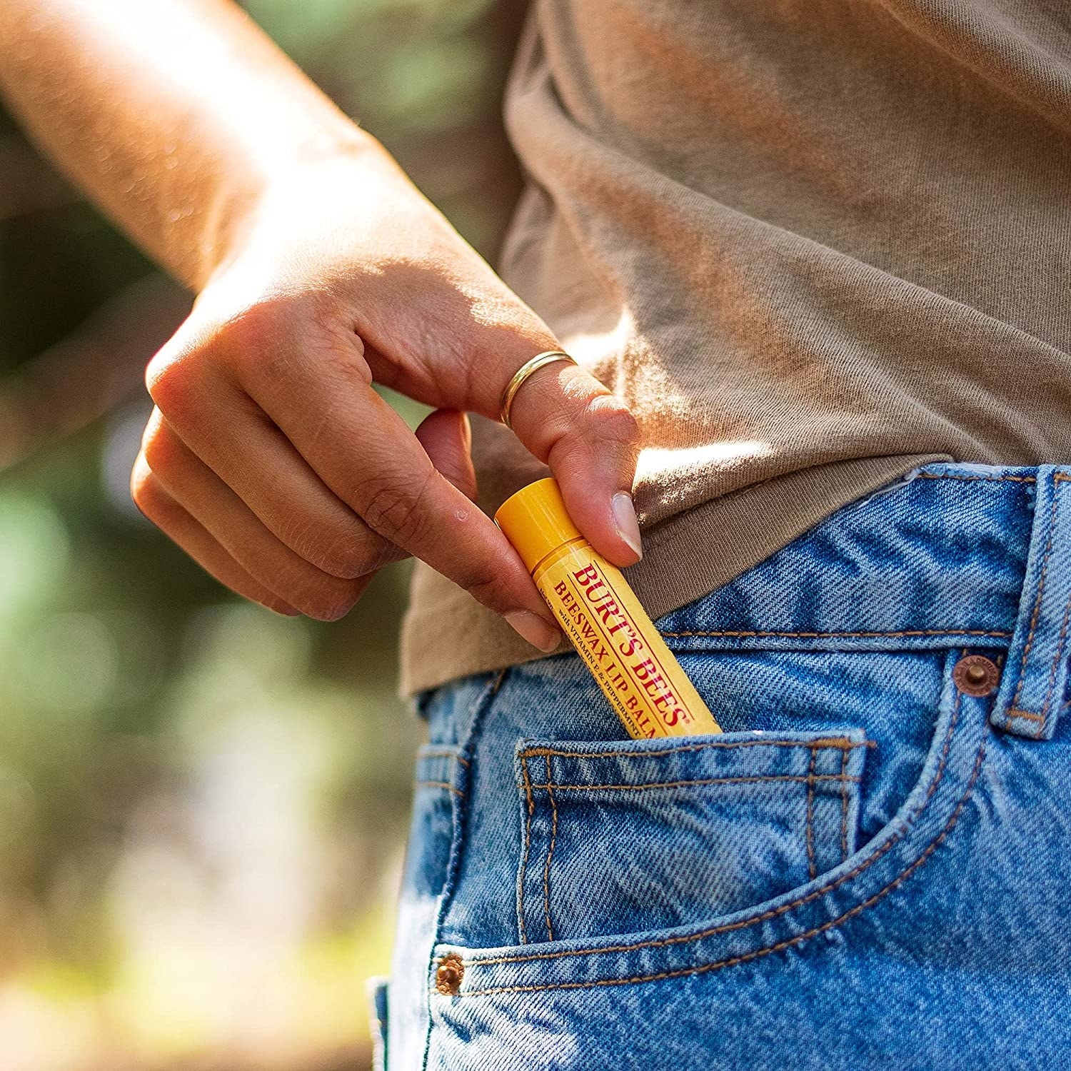 hand pulls Burt's Bees lip balm tube out of jean pocket