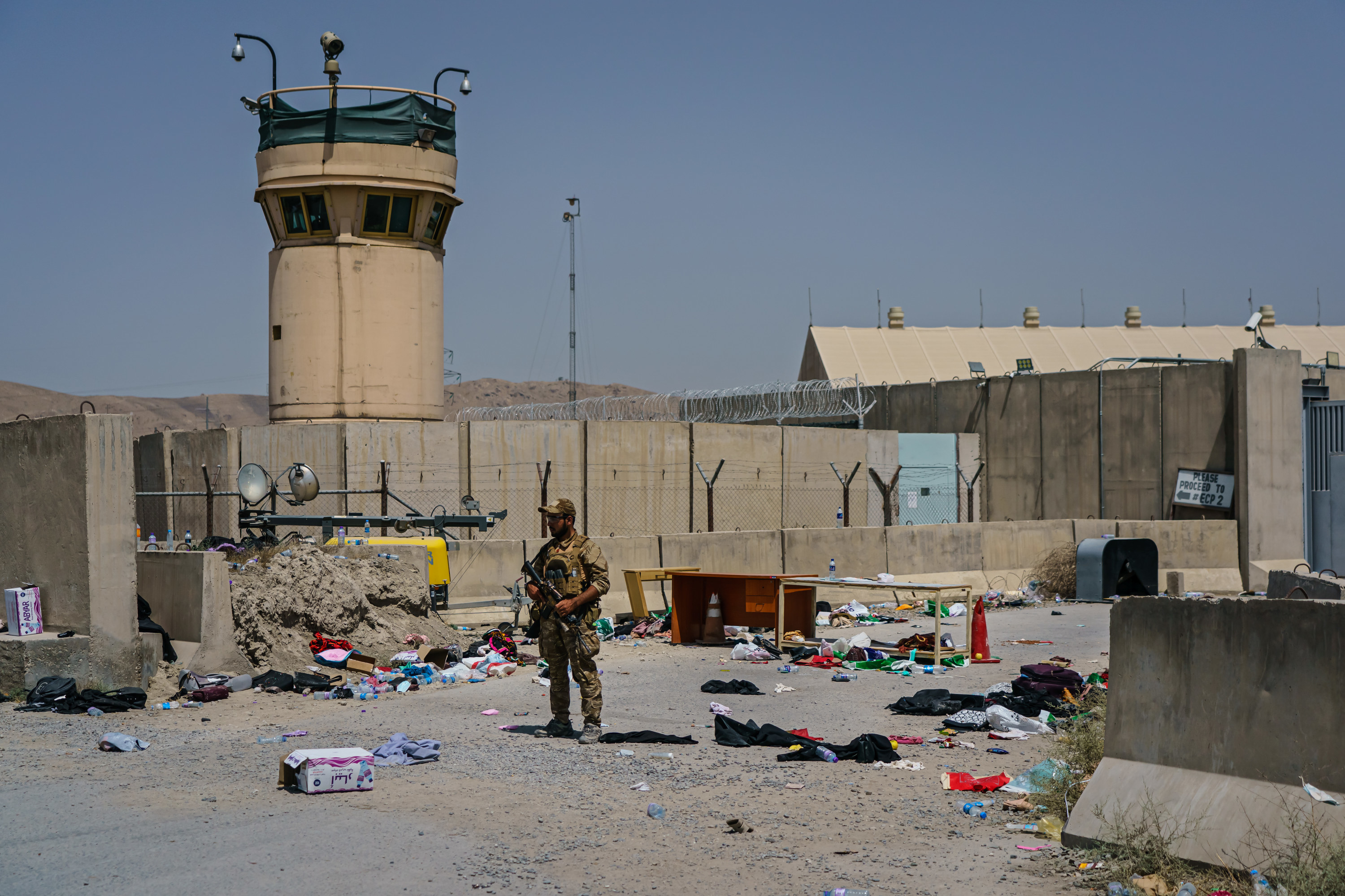 A soldier is surrounded by belongings and debris as he stands guard outside an airport 