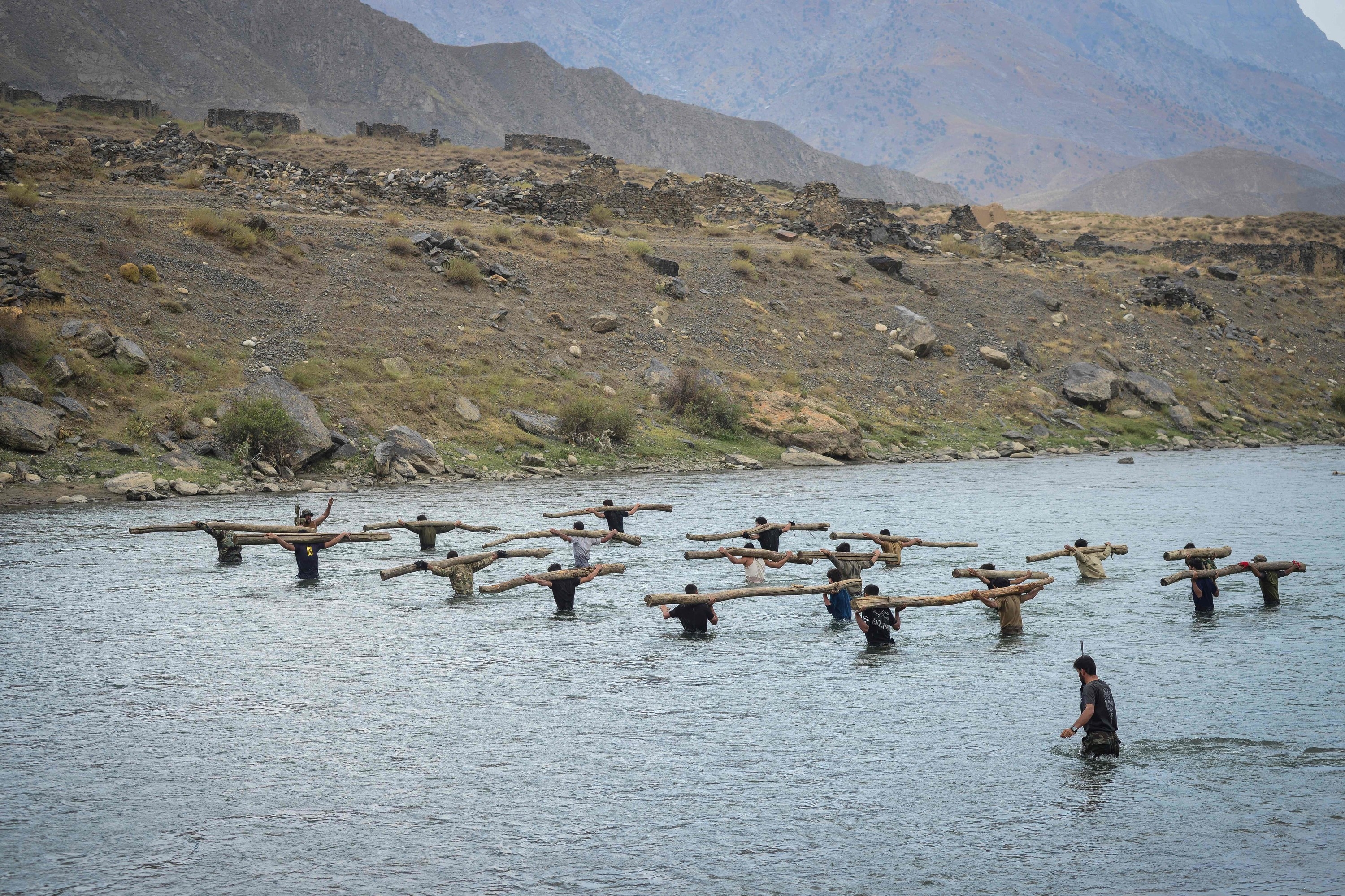 Anti-Taliban resistance soldiers train by carrying logs as they walk through water