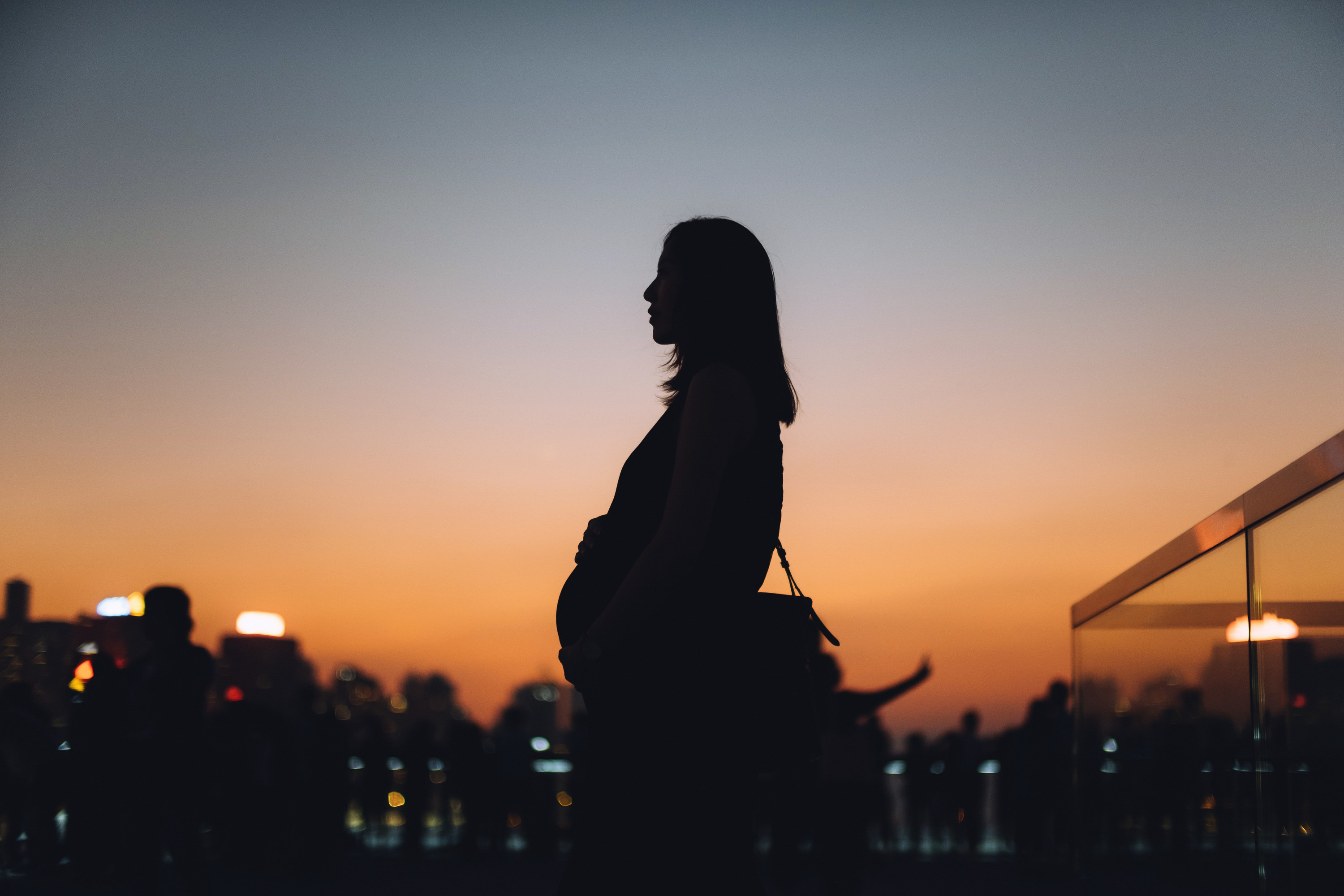 An image of a woman holding her pregnant stomach in front of a setting sun