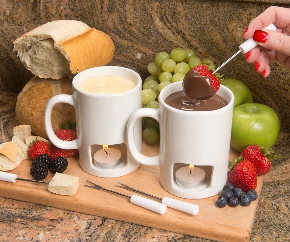 a model dipping a strawberry into a mug filled with chocolate fondue with a tea candle in the bottom compartment of the mug