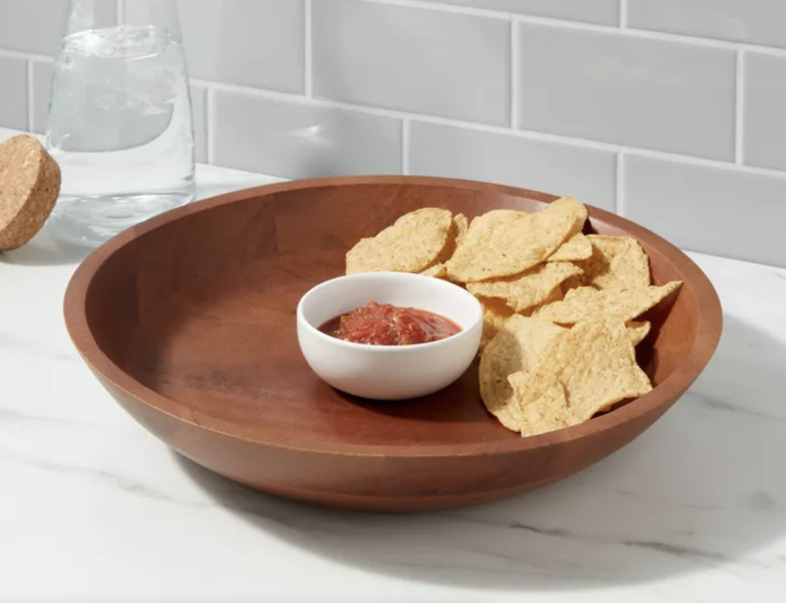 A wooden bowl full of chips with a white glass bowl of salsa in the middle