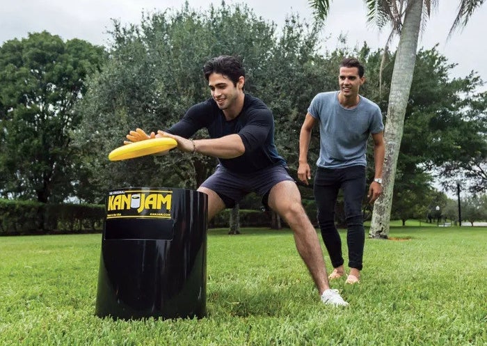 a model slapping a yellow frisbee into a black Kan Jam bin