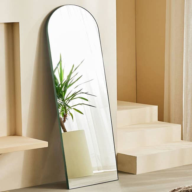 full length mirror with arch at top. it is leaning against a wall and has a green outer frame.