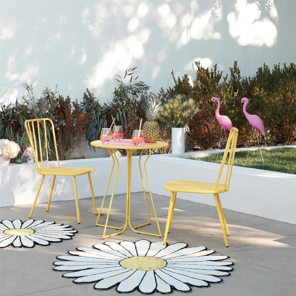 bright yellow chair and table sitting outside next to a daisy-shaped rug
