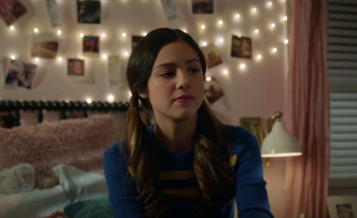 Olivia Rodrigo is sitting on a bed, looking sad