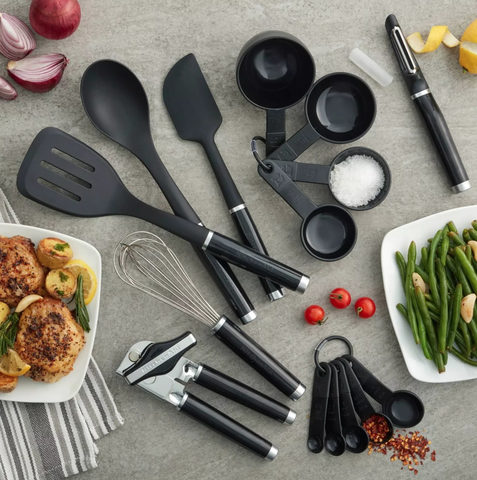 the utensil set on a gray counter with various plates of food and spices surrounding it.