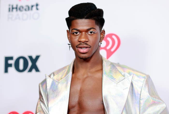 Lil Nas in a metallic jacket sans shirt with matching eyeliner and several earrings