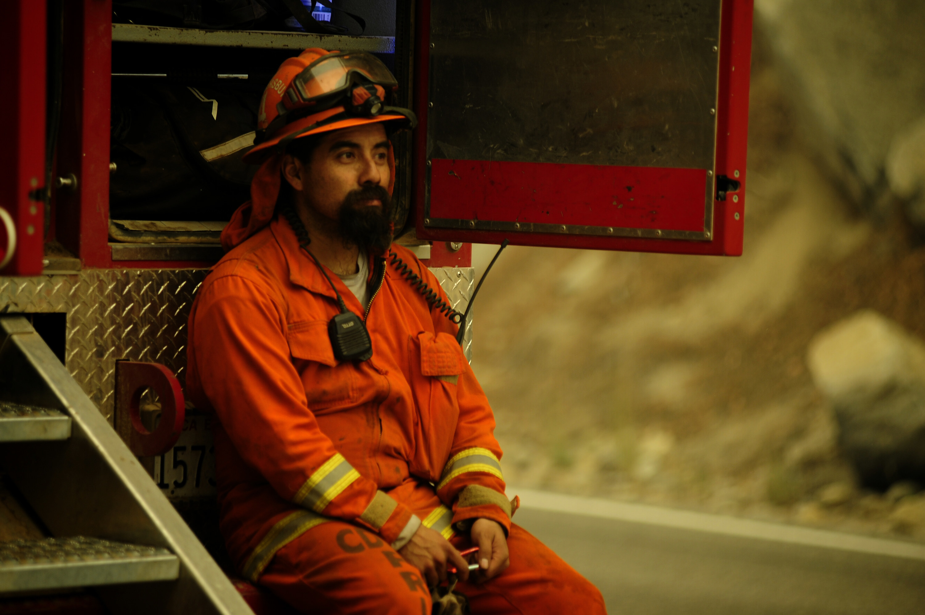 A firefighter in uniform sits on the back of a truck